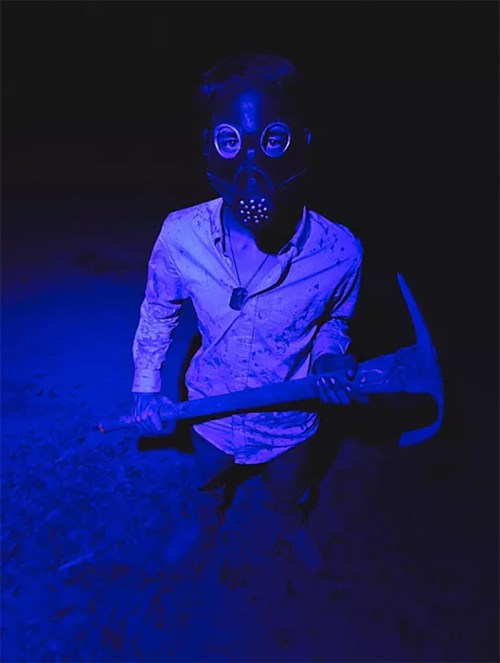 A person in a gas mask holds a pickaxe, standing in a dark, blue-lit environment.