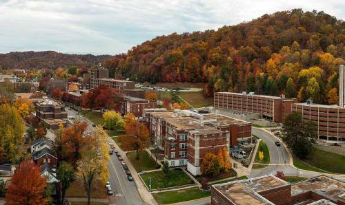 Aerial view of a college campus surrounded by vibrant autumn foliage and rolling hills.
