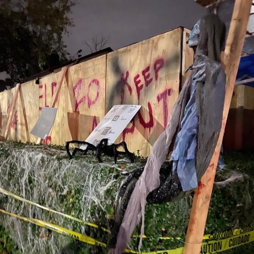 A spooky scene with a ghostly figure hanging near a fence marked with "KEEP OUT" and cobwebs, set at night.