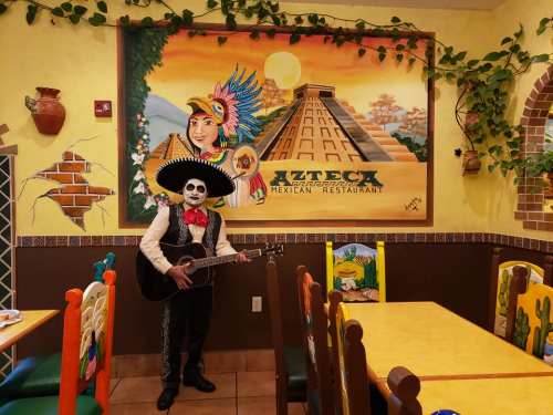 A musician in a sombrero and suit plays guitar in a colorful Mexican restaurant with vibrant wall art.