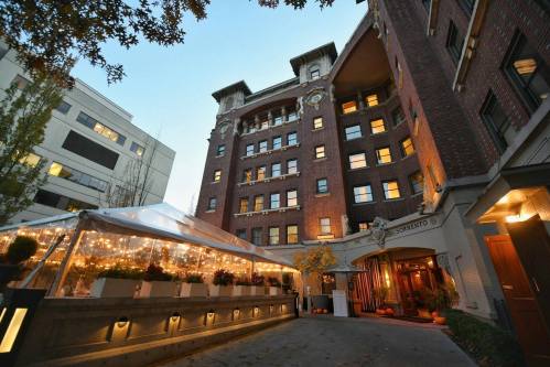 A charming brick building with a tented outdoor area, illuminated by string lights, set against a twilight sky.