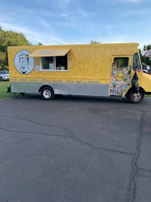 A bright yellow food truck with a cartoon chef logo, serving grilled cheese and other comfort foods.
