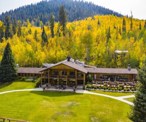 A spacious lodge surrounded by vibrant autumn trees and a green lawn, set against a mountain backdrop.