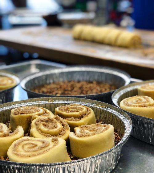 Cinnamon rolls in aluminum pans, ready for baking, with a rolling pin in the background.