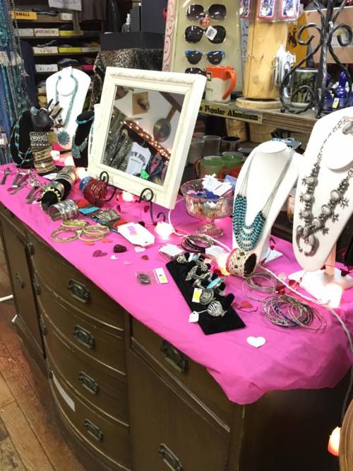 A display of jewelry on a pink tablecloth, featuring necklaces, bracelets, and rings in a shop setting.