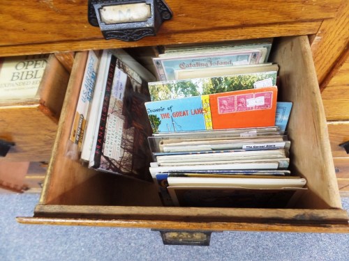 A wooden drawer filled with various old postcards and brochures, showcasing a collection of vintage travel memorabilia.