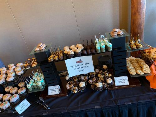 A dessert table featuring cupcakes, cookies, and assorted treats with a sign inviting guests to be served.