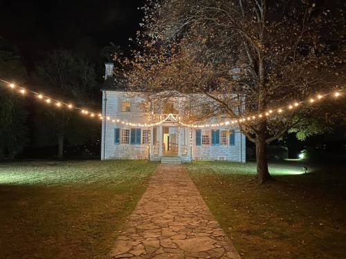A charming house at night, illuminated by string lights, with a stone pathway leading to the entrance and bare trees nearby.
