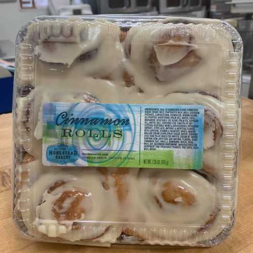 A clear plastic container filled with frosted cinnamon rolls, labeled "Cinnamon Rolls" from Homestead Bakery.