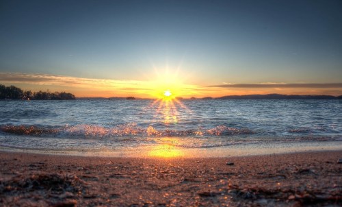 A serene beach at sunset, with gentle waves lapping at the shore and a vibrant sun setting over the horizon.