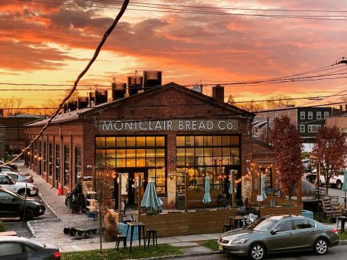 A brick bakery with large windows, "Montclair Bread Co." sign, surrounded by outdoor seating and a vibrant sunset sky.