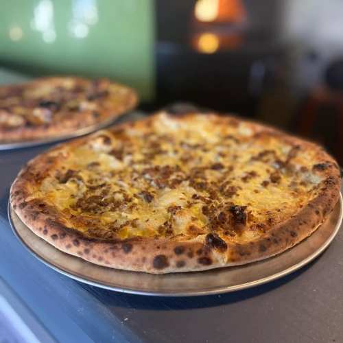 A close-up of a golden-brown pizza on a metal plate, topped with melted cheese and savory toppings.