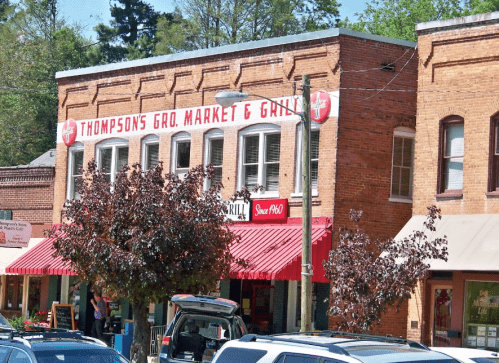 A brick building with a red awning, featuring a sign for "Thompson's Gro. Market & Grill" and surrounding trees.