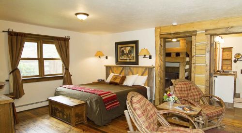 Cozy room with a bed, wooden furniture, and a seating area, featuring rustic decor and warm lighting.
