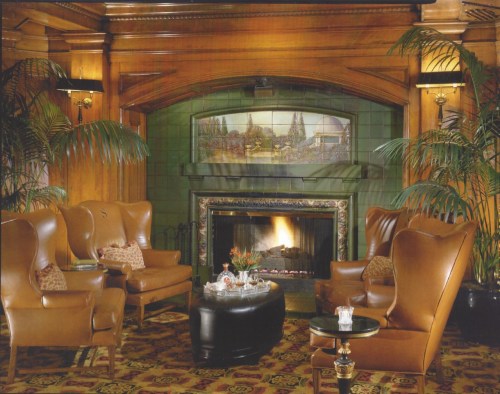 Cozy lounge with two brown armchairs, a fireplace, and decorative plants, featuring warm wood paneling and a patterned rug.