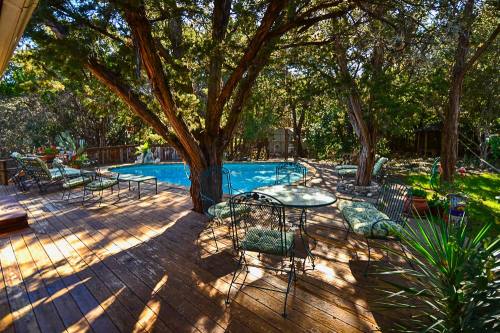 A serene backyard with a wooden deck, pool, and shaded seating area surrounded by trees and greenery.