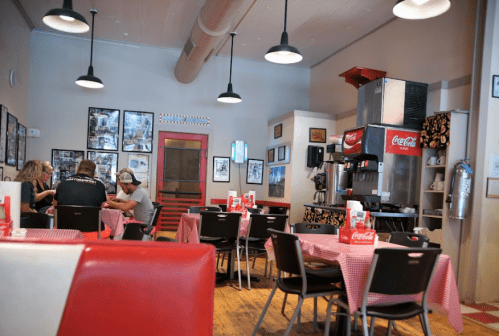 A cozy diner with red and white decor, checkered tablecloths, and customers enjoying their meals at tables.