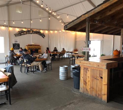 A cozy indoor space with string lights, tables, and people enjoying drinks, featuring a wooden bar and seasonal decor.