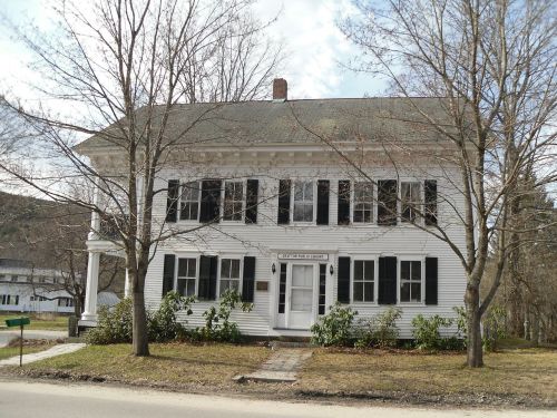 A large white two-story house with black shutters, surrounded by bare trees and a grassy lawn.