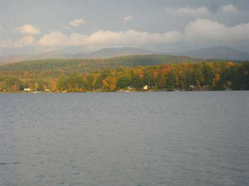 A serene lake surrounded by colorful autumn trees and distant mountains under a cloudy sky.