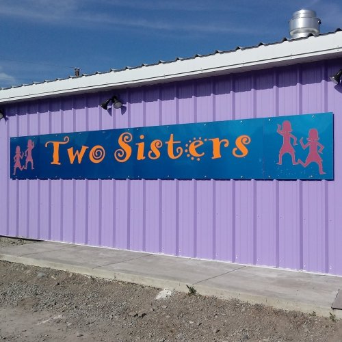 A colorful sign on a purple wall reads "Two Sisters," featuring playful silhouettes of two girls.