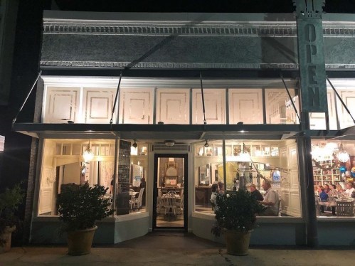 A cozy restaurant at night, with warm lights and people dining inside, featuring large windows and an "OPEN" sign.