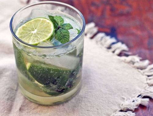 A refreshing cocktail with lime slices and mint leaves, served over ice in a glass on a textured surface.