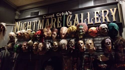 A wall display featuring various creepy masks and skulls under the sign "Count Orlok's Nightmare Gallery."