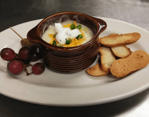 A bowl of creamy dessert topped with coconut and orange, served with cookies and grapes on a white plate.