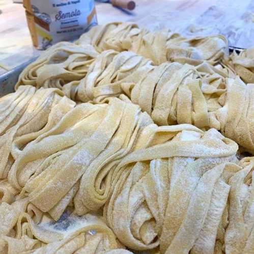 Freshly made pasta strands piled together, dusted with flour, on a wooden surface.