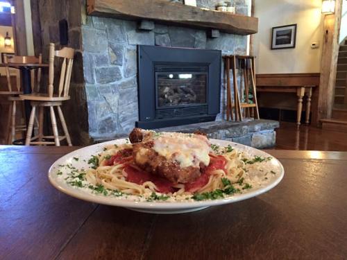 A plate of pasta with chicken, marinara sauce, and cheese, set in a cozy restaurant with a stone fireplace in the background.