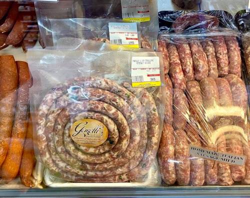 A display of various sausages, including a large coil and packaged links, in a butcher shop.