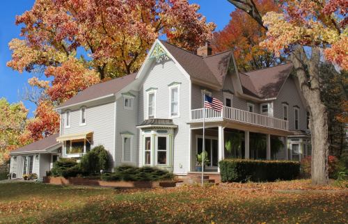 A charming white house surrounded by vibrant autumn trees and fallen leaves, featuring a porch and an American flag.