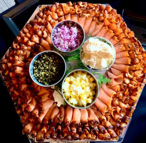 A hexagonal platter filled with rolled salmon, garnished with bowls of onions, cream cheese, and chopped eggs.