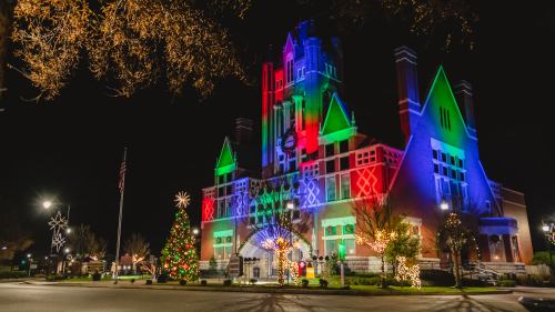 A brightly lit building adorned with colorful holiday lights, surrounded by festive decorations and a Christmas tree.