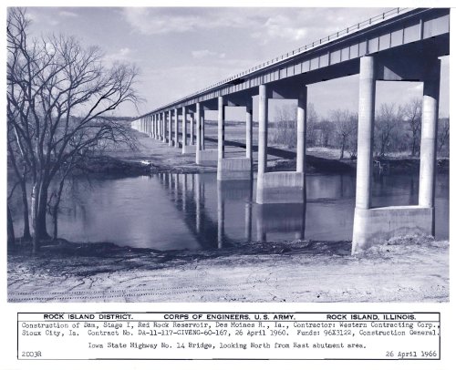 Black and white photo of a bridge under construction over a river, with a highway visible in the foreground.