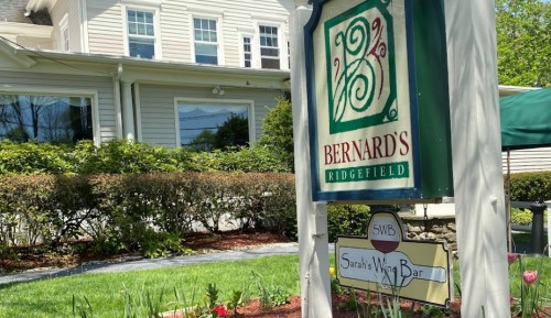 Sign for Bernard's Ridgefield and Sarah's Wine Bar, with a green lawn and blooming flowers in the foreground.