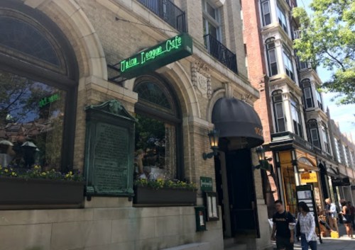 Exterior of Union League Café, featuring a green sign and people walking by on a sunny day.