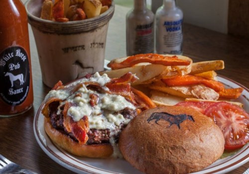 A plate featuring a bacon cheeseburger with sauce, tomato, and a side of fries, alongside a bottle of hot sauce.