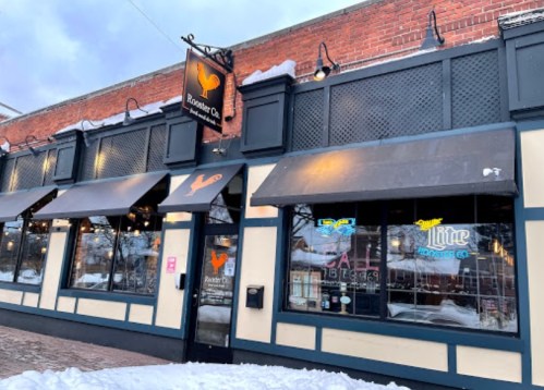 Exterior of a restaurant with a rooster logo, snow on the ground, and awnings over the windows.