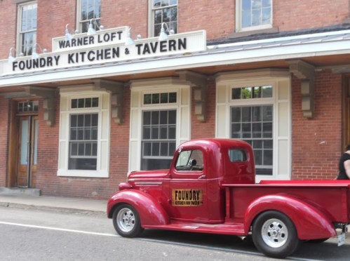 A vintage red truck parked in front of the Warner Loft Foundry Kitchen & Tavern building.