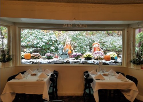 A cozy restaurant interior with two tables set for dining, featuring a window view of autumn decorations and pumpkins outside.