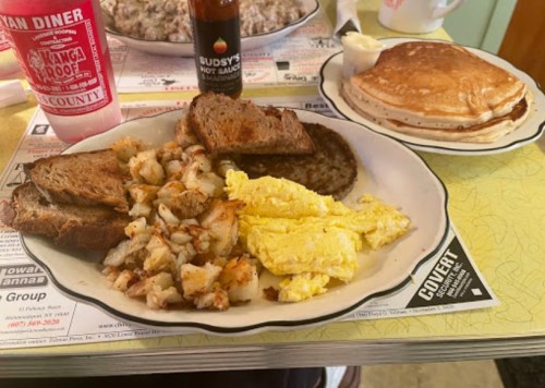 A plate of breakfast featuring scrambled eggs, sausage, hash browns, toast, and a side of pancakes.