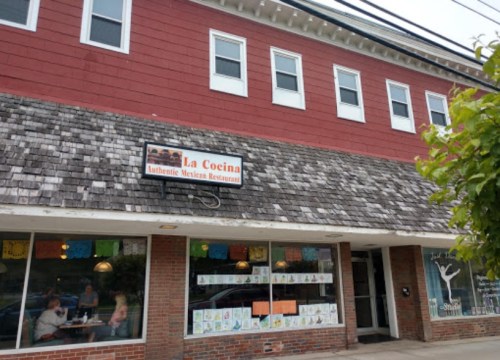 Exterior of La Cocina, an authentic Mexican restaurant, featuring a shingled roof and colorful decorations in the windows.