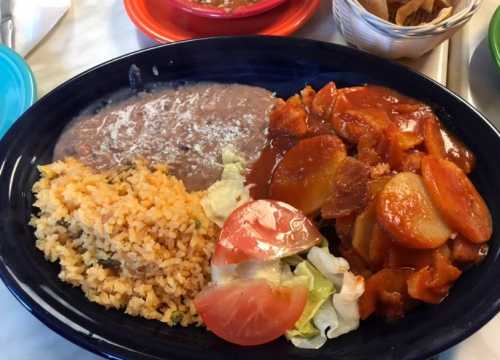 A plate of food featuring rice, refried beans, lettuce, tomato, and a sweet and sour chicken dish.