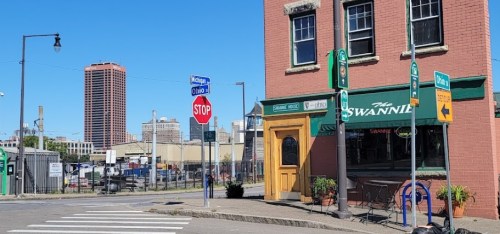 A street view of a brick building with a pub sign, a stop sign, and city skyline in the background under a clear blue sky.