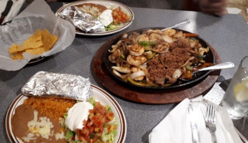 A sizzling platter of shrimp and beef fajitas with onions, served with rice, beans, salad, and tortilla chips.