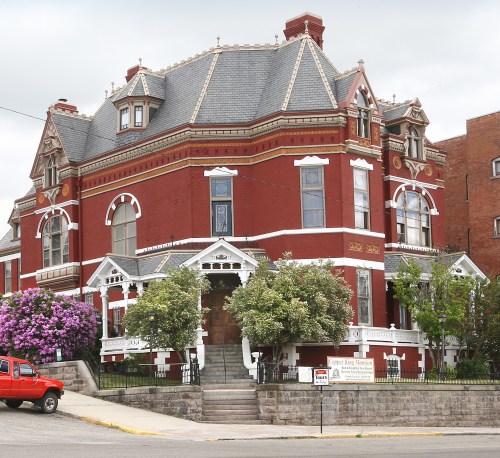 A large, ornate red brick mansion with intricate architectural details and lush greenery in front.