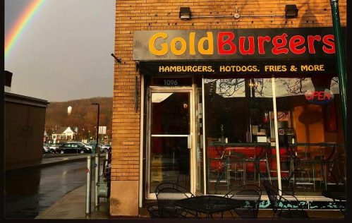 A restaurant called "GoldBurgers" with a rainbow in the background, featuring outdoor seating and a welcoming sign.