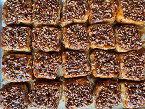 A tray of freshly baked sticky buns topped with caramel and chopped pecans.